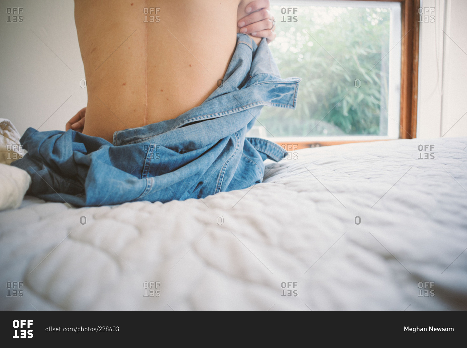 A Woman Taking Off Her Shirt While Siting On The Edge Of A Bed Stock Photo OFFSET