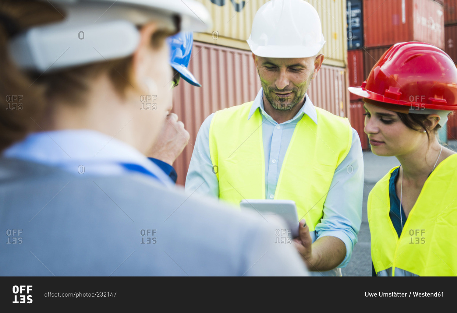 Four people with safety helmets and digital tablet talking at container port