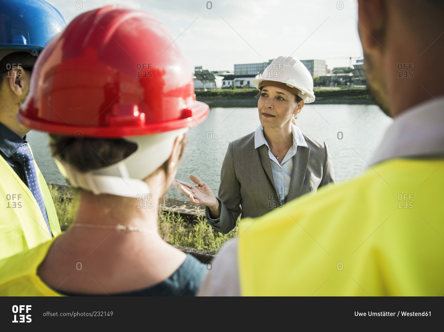 Businesswoman talking to people with safety helmets at riverside