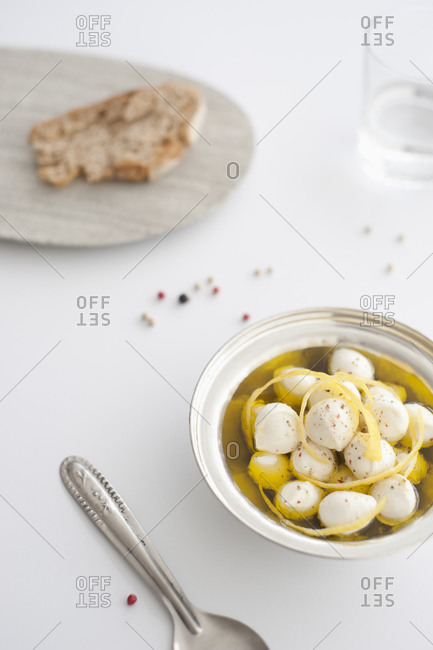 Fresh mozzarella balls in olive oil with cracked pepper and lemon rind on white background