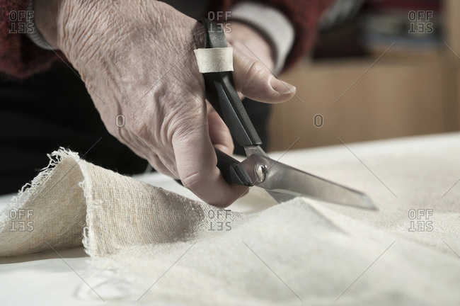 Senior female fashion designer cutting fabric with scissors in workshop