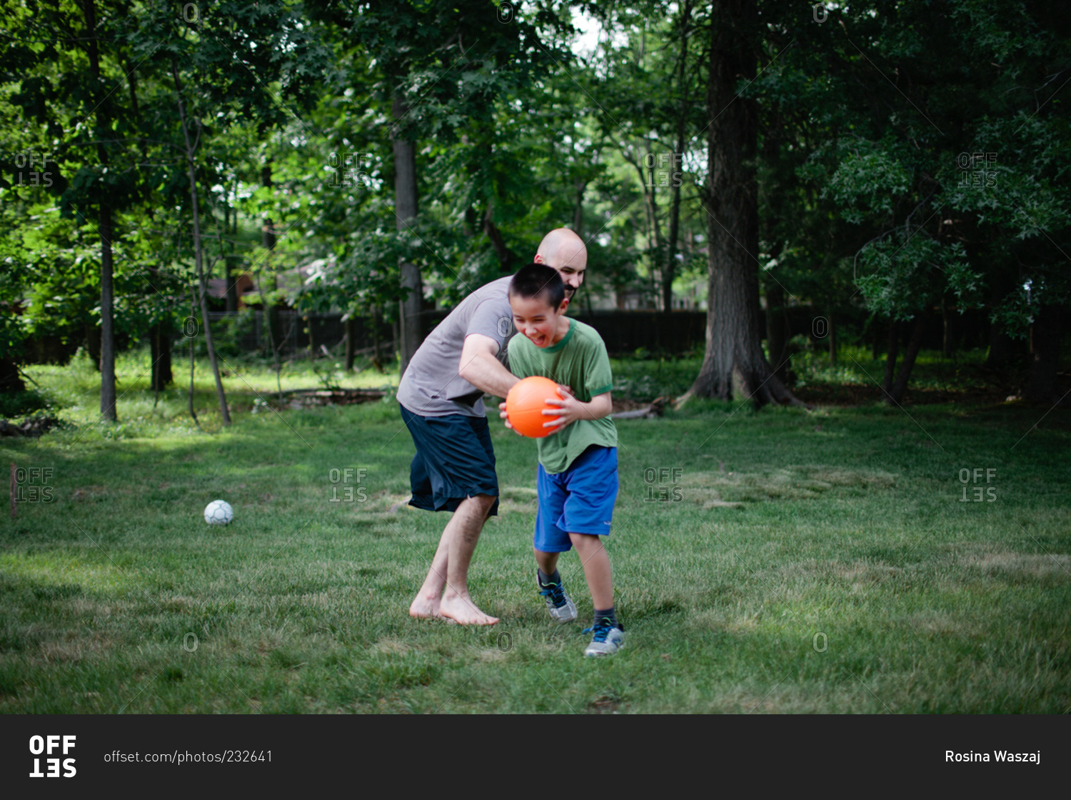 Dad and boy wrestling over ball in yard