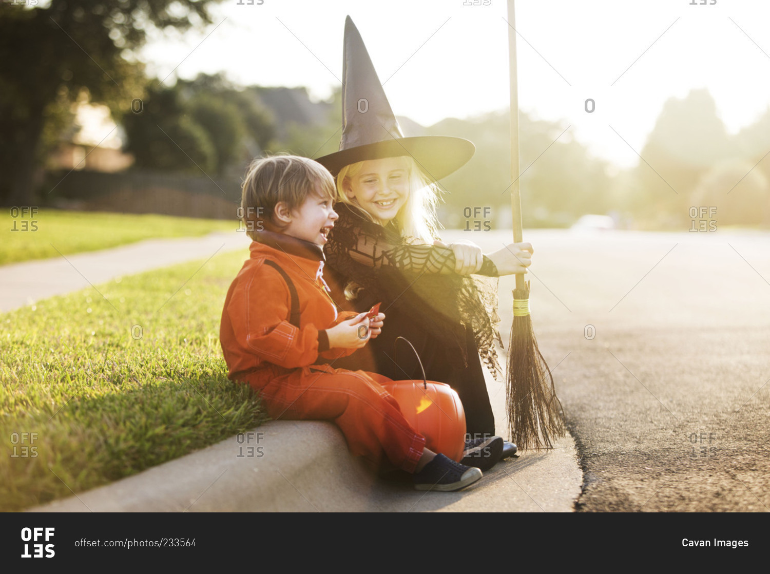 Siblings sitting on a roadside in Halloween costumes