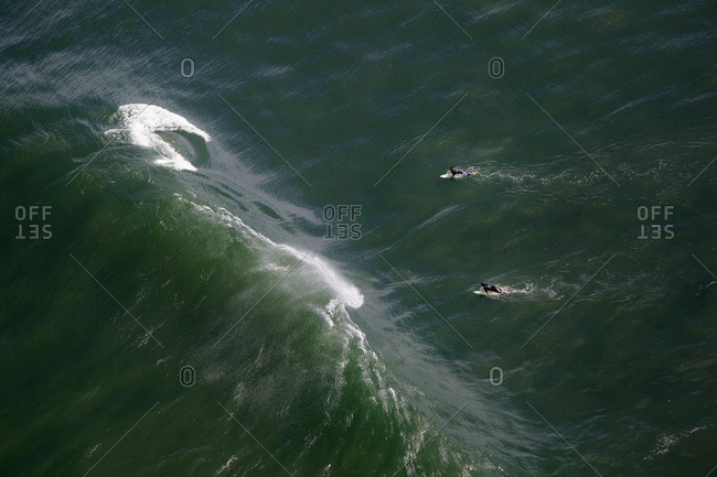 Two surfers paddle under a wave as the surf under near the Golden Gate Bridge in San Francisco, CA