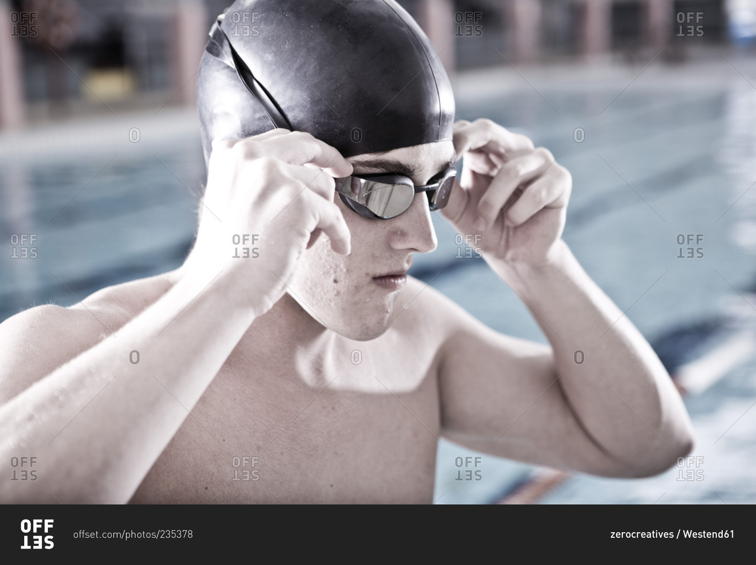 Swimmer in indoor pool putting on swimming goggles