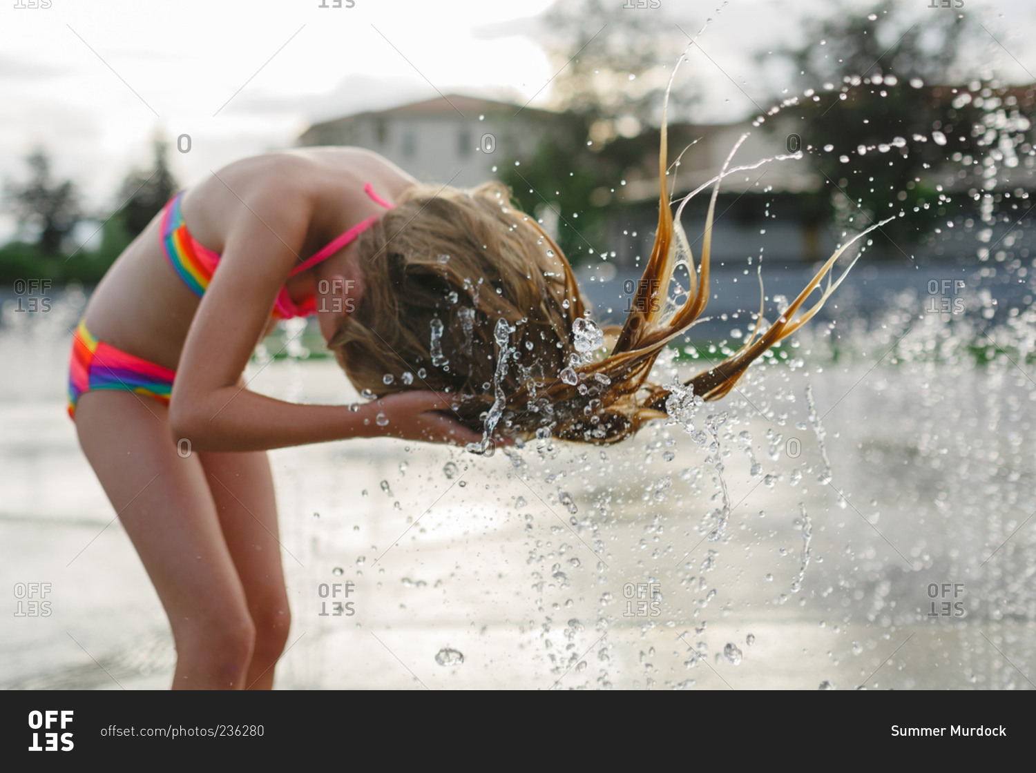 Girl whipping wet hair in city fountain
