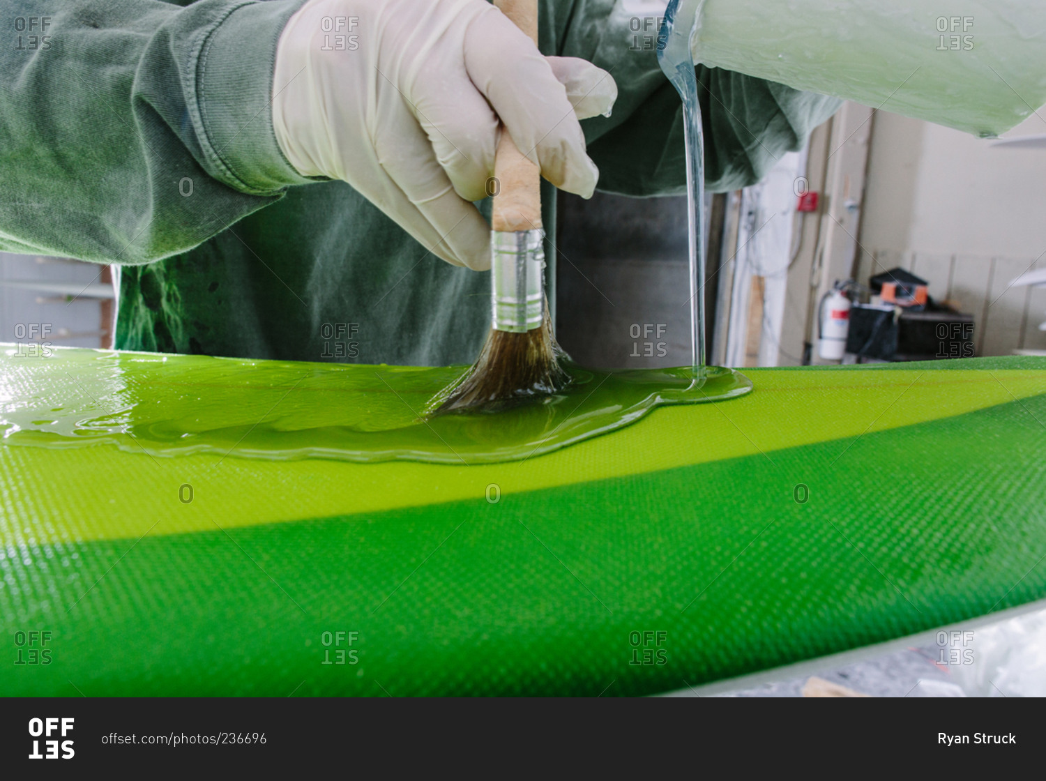 Pouring the glaze coating on a green surfboard in a surf shop stock