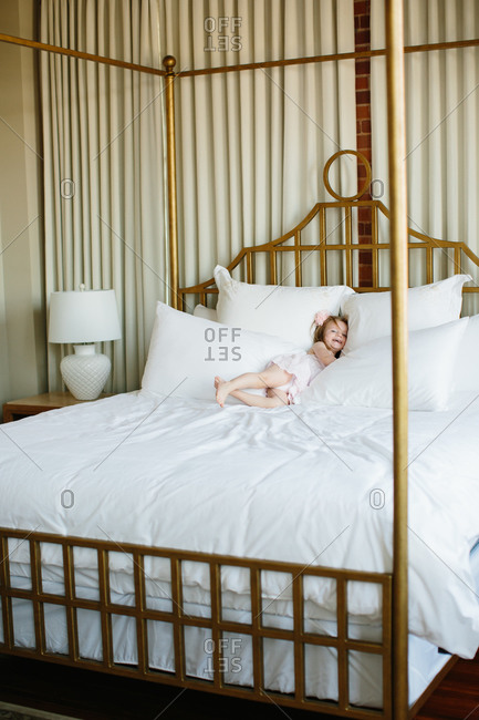 Toddler girl rolling in plush white bedding of a brass bed stock
