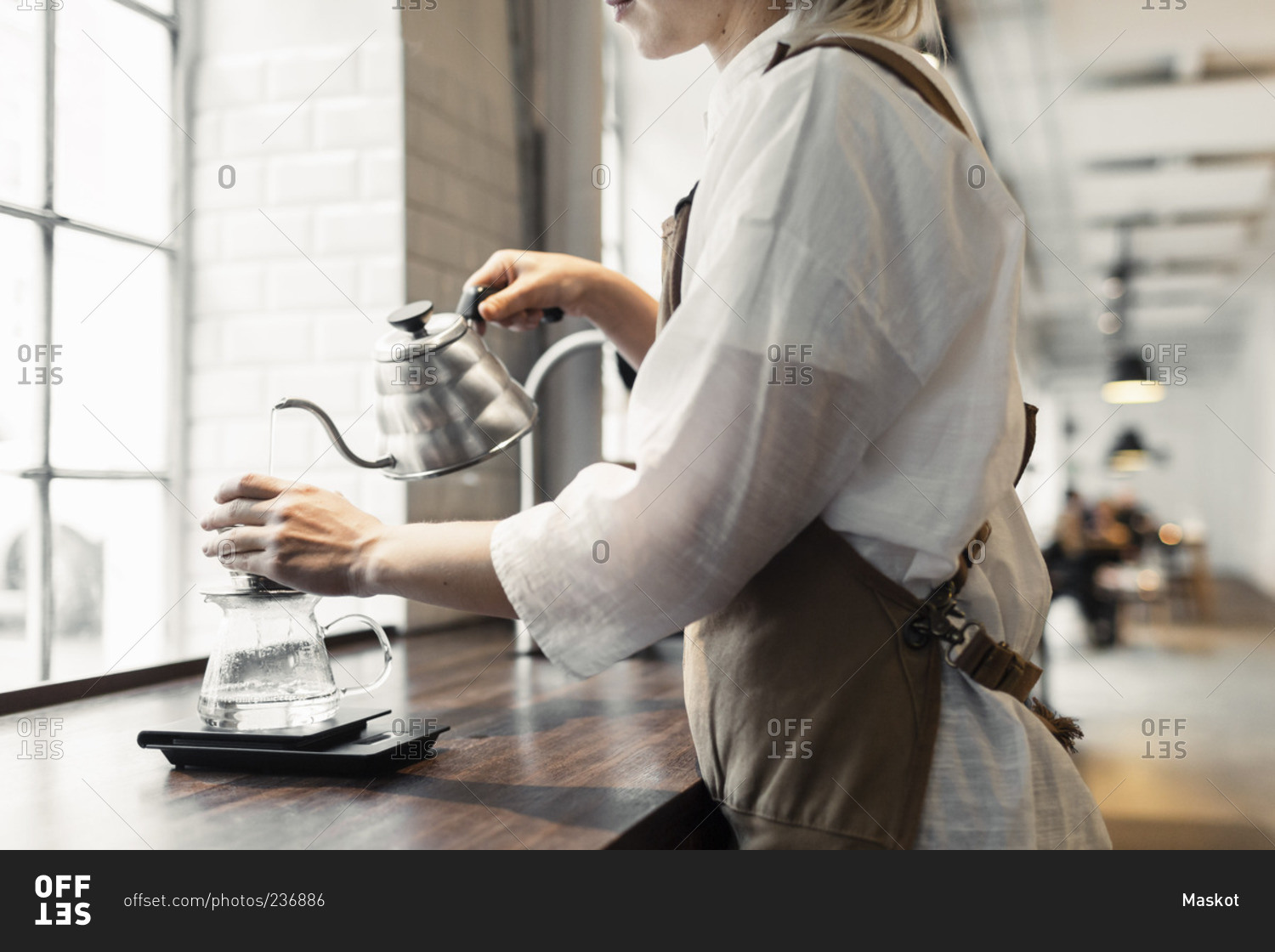 Female barista pouring boiling water in coffee filter at cafe counter