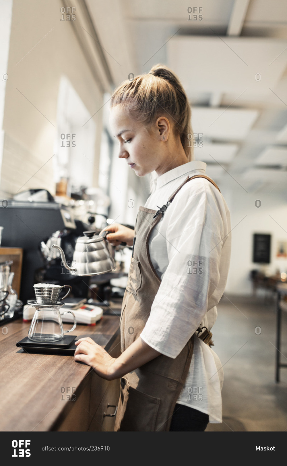 Side view of young female barista making coffee at counter