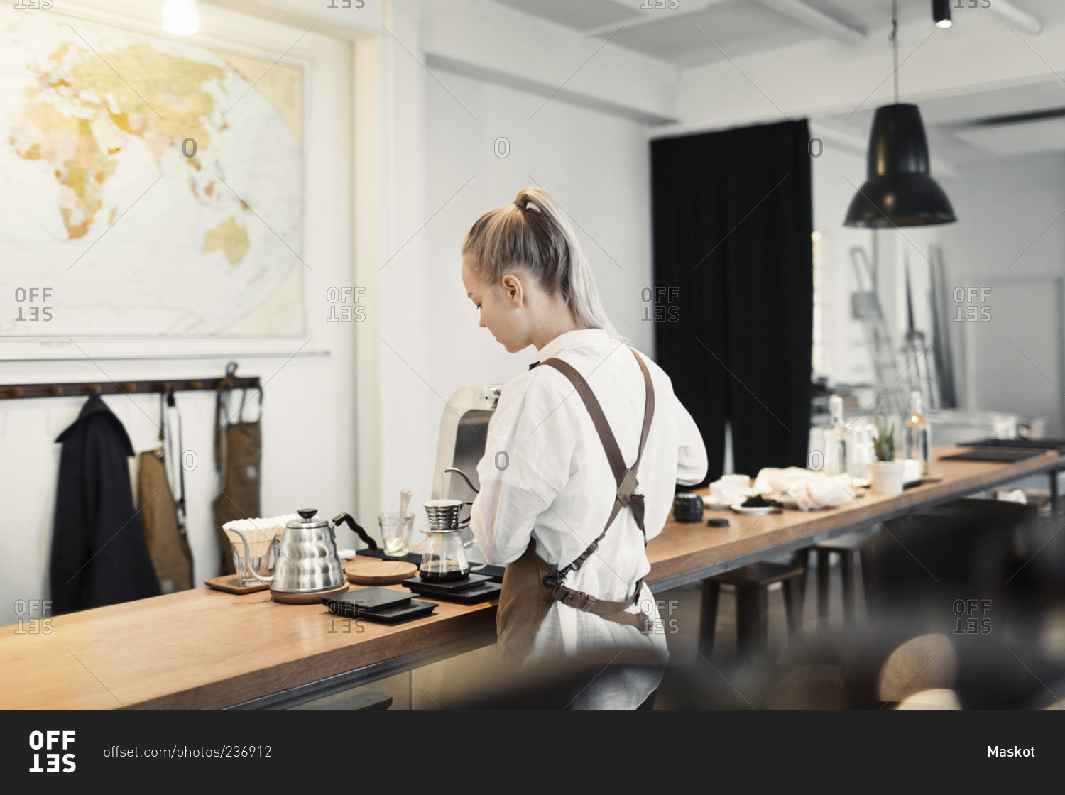 Rear view of young female barista preparing coffee at counter