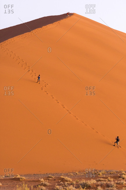 Two people walk down a sand dune in the Namibian desert