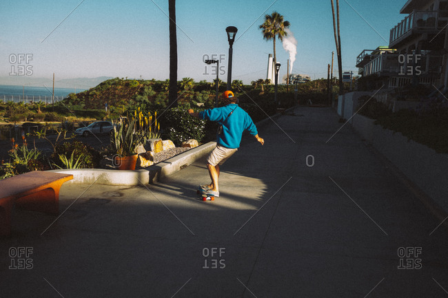 Man riding skateboard along a sidewalk in a coastal town