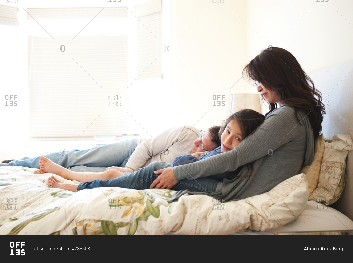 Girl lounging with her parents on their bed in sunny room stock photo ...