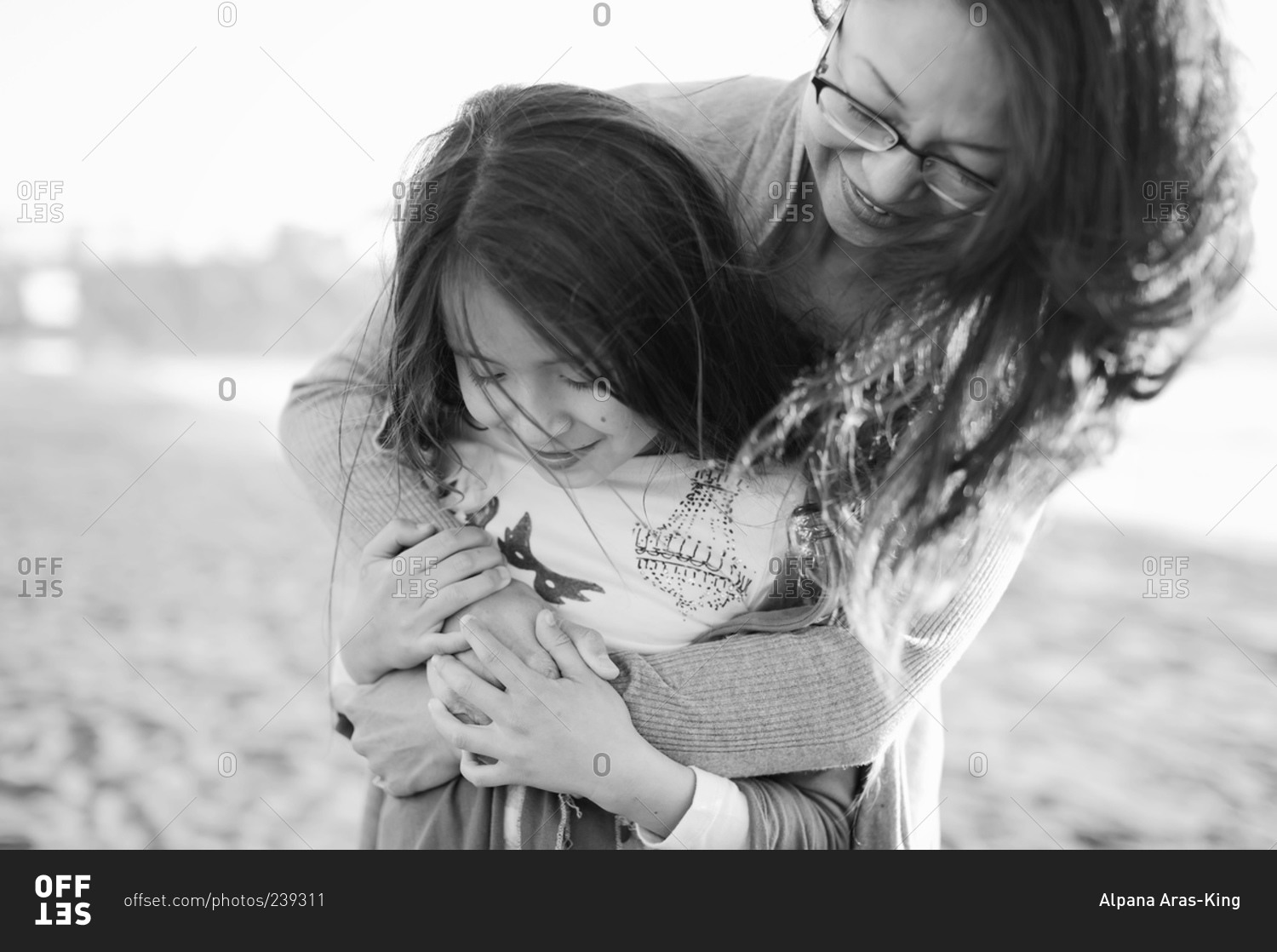 Portrait Of Mother Hugging Her Daughter From Behind At The Beach Stock 