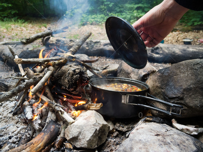 Lid being removed from a pot of soup on a campfire