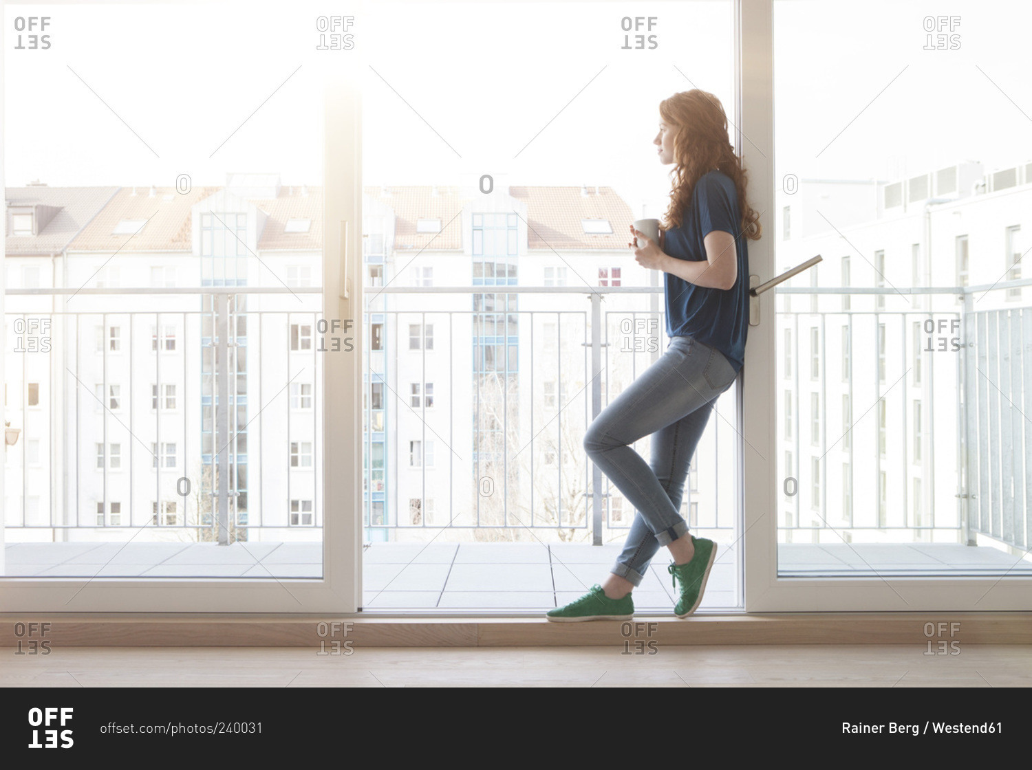 Young woman leaning at sliding door of balcony looking at distance stock photo OFFSET