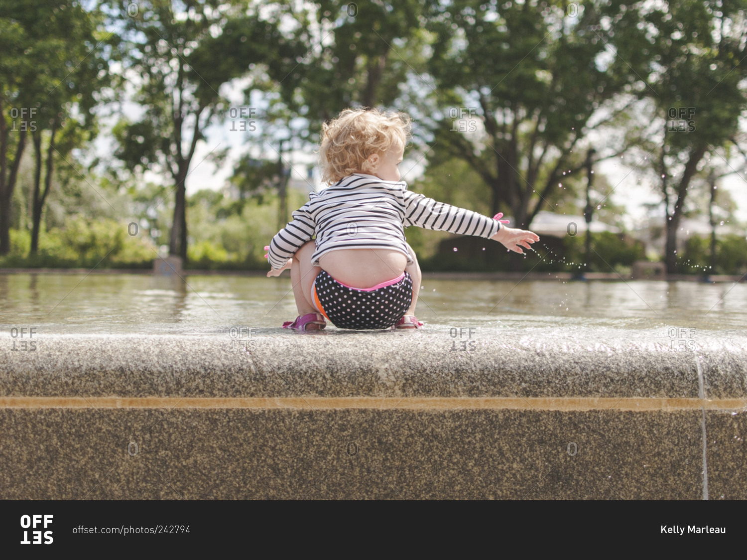 A little girl sits on the edge of a fountain