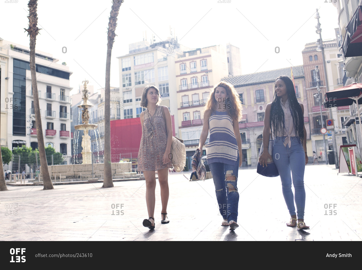 Three women walk past a fountain in a Spanish city square