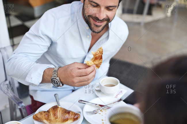 Man eating a croissant at an outdoor caf_