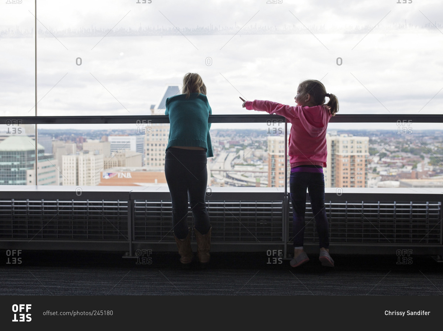 Two kids looking out window at city view stock photo - OFFSET