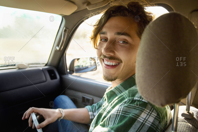 A young man sit in the front seat of a car smiling