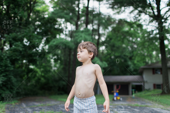 Shirtless young boy standing in driveway at home stock photo - OFFSET