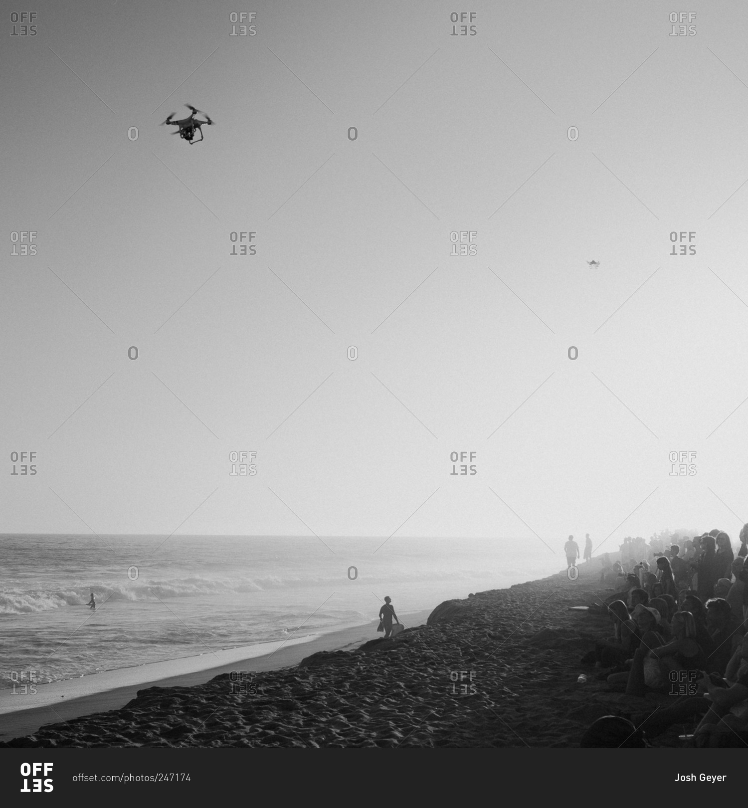 Drones in flight above a crowd sitting on beach at surf competition