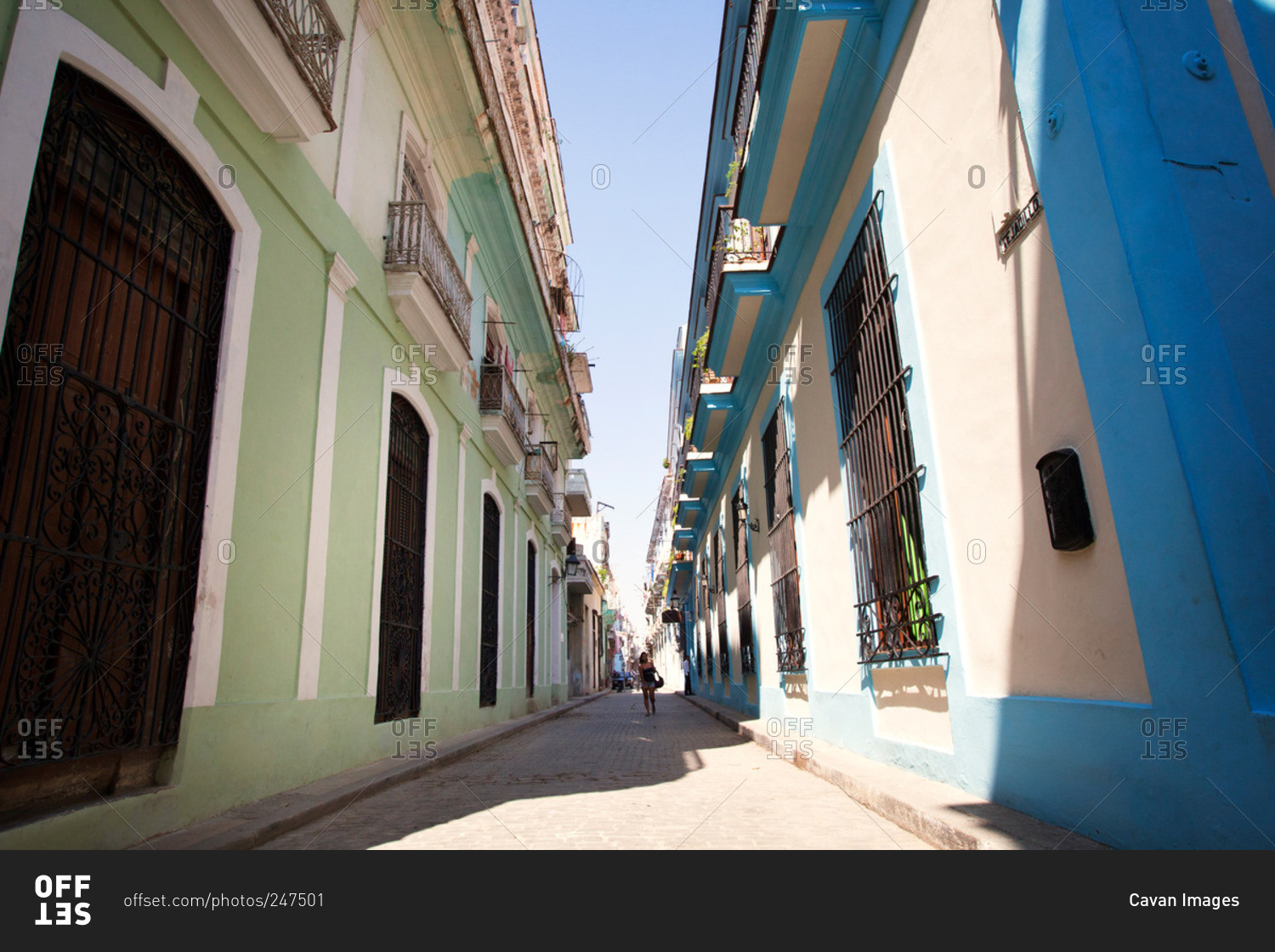 Woman walking down narrow alley with green and blue painted buildings on either side