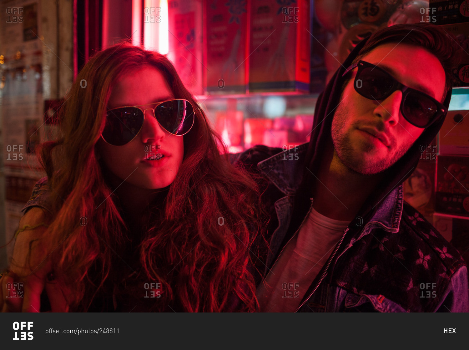 Hip young couple lit by neon lights wearing sunglasses at night