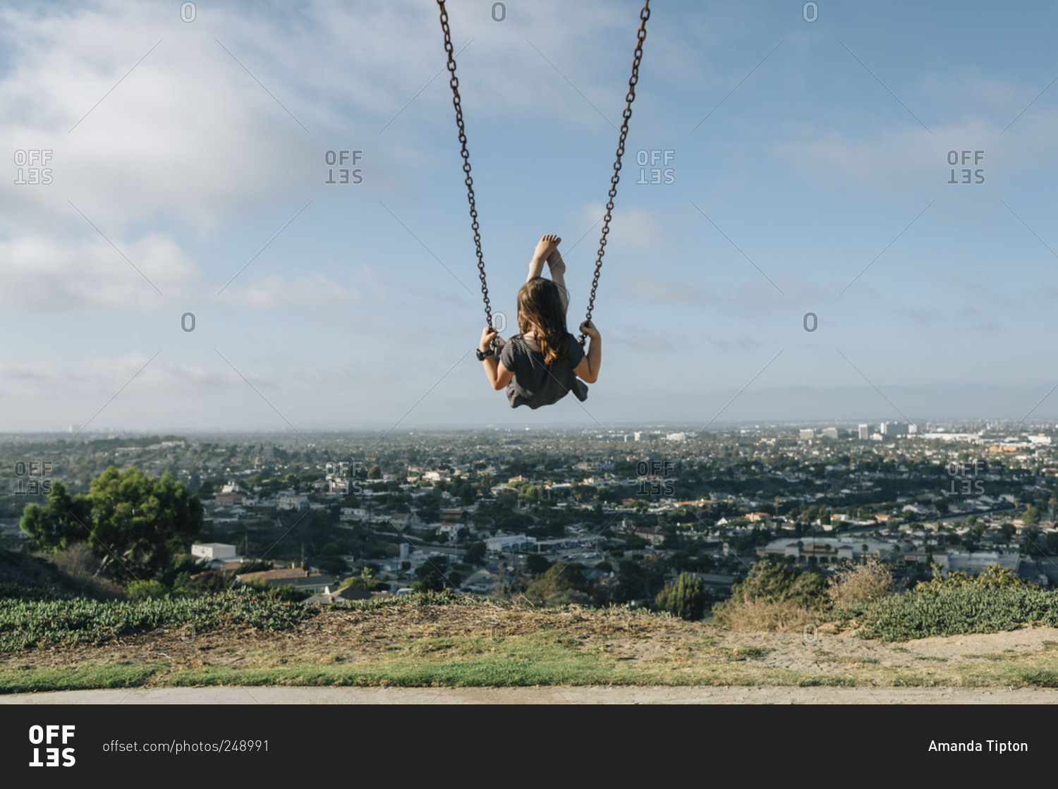 Girl on swing on hill overlooking city stock photo - OFFSET