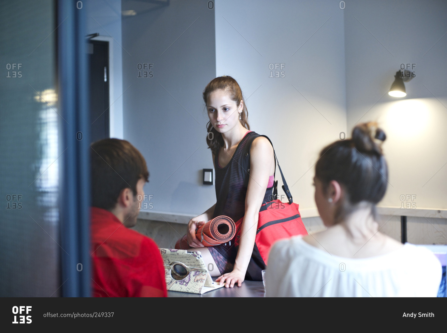 Woman with yoga mat talking to colleagues stock photo OFFSET