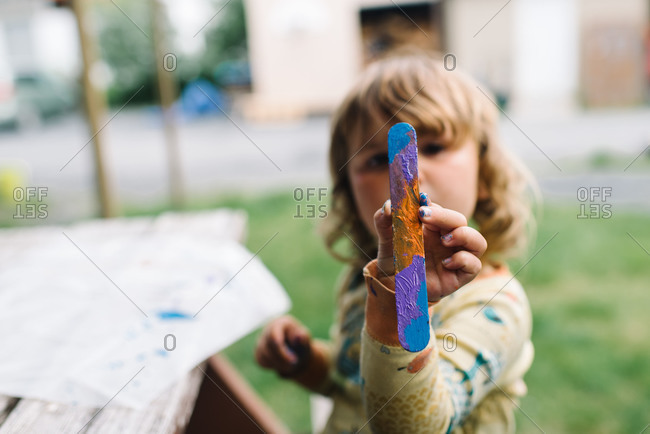 Little girl holding up painted popsicle stick
