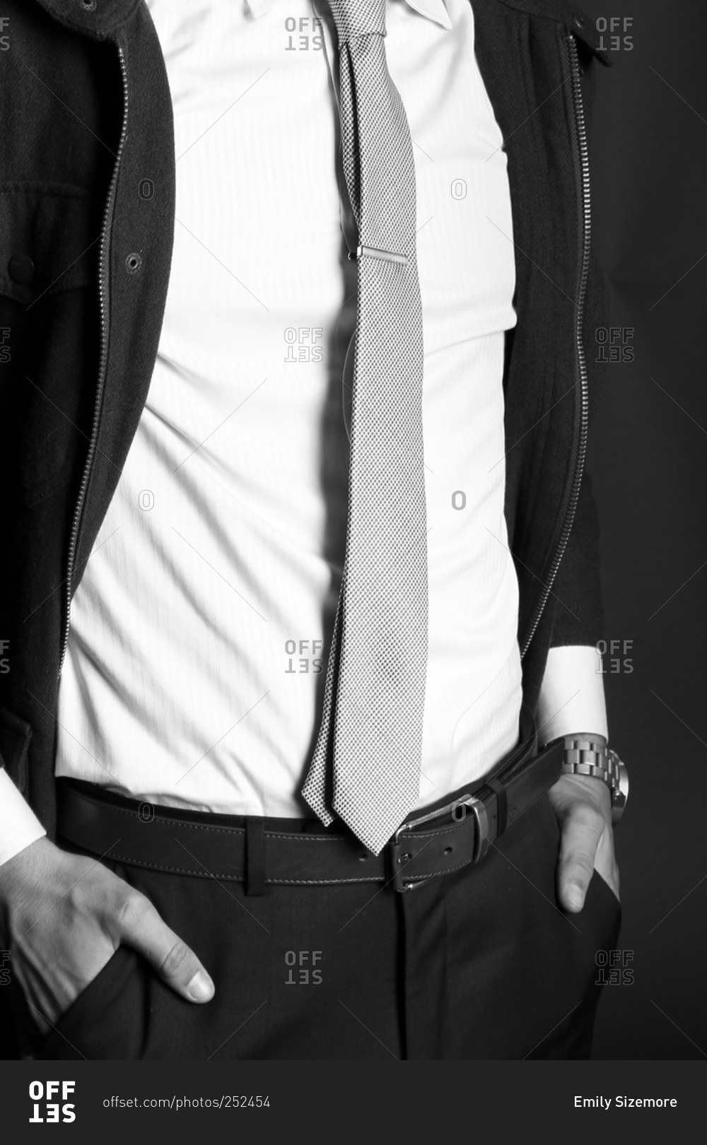 Fashion shot of man wearing a zip jacket with white shirt, tie, and black pants