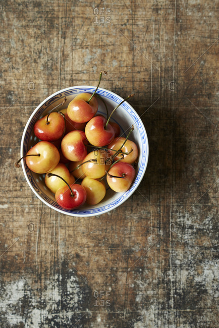 A bowl of Rainier cherries on a textured metal surface