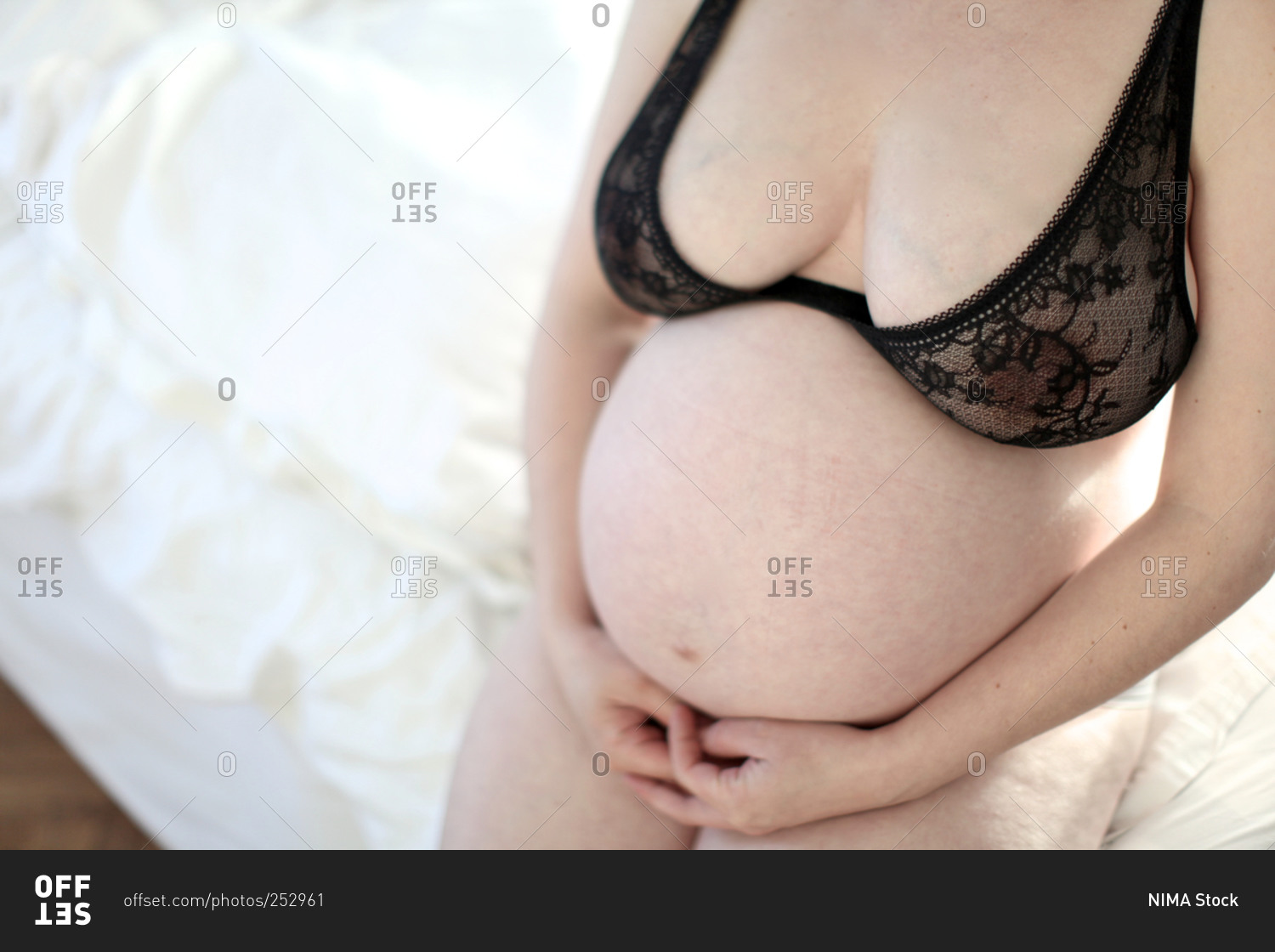 Pregnant woman with black underwear sitting on bed stock photo - OFFSET