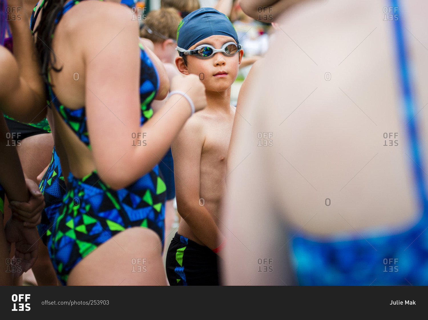 A boy in swimming goggles stands in a crowd of swimmers