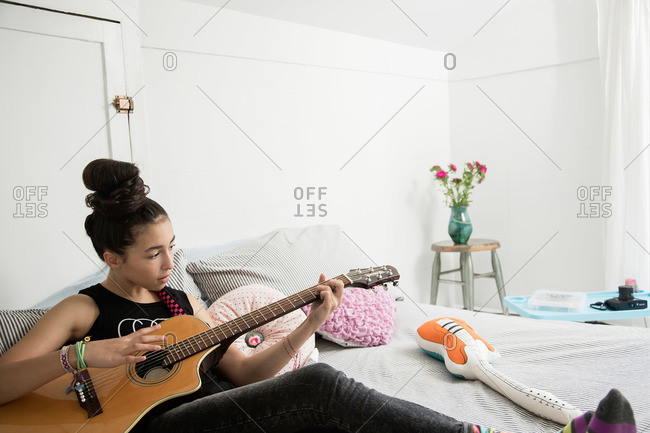 Girl sitting on her bed playing a guitar
