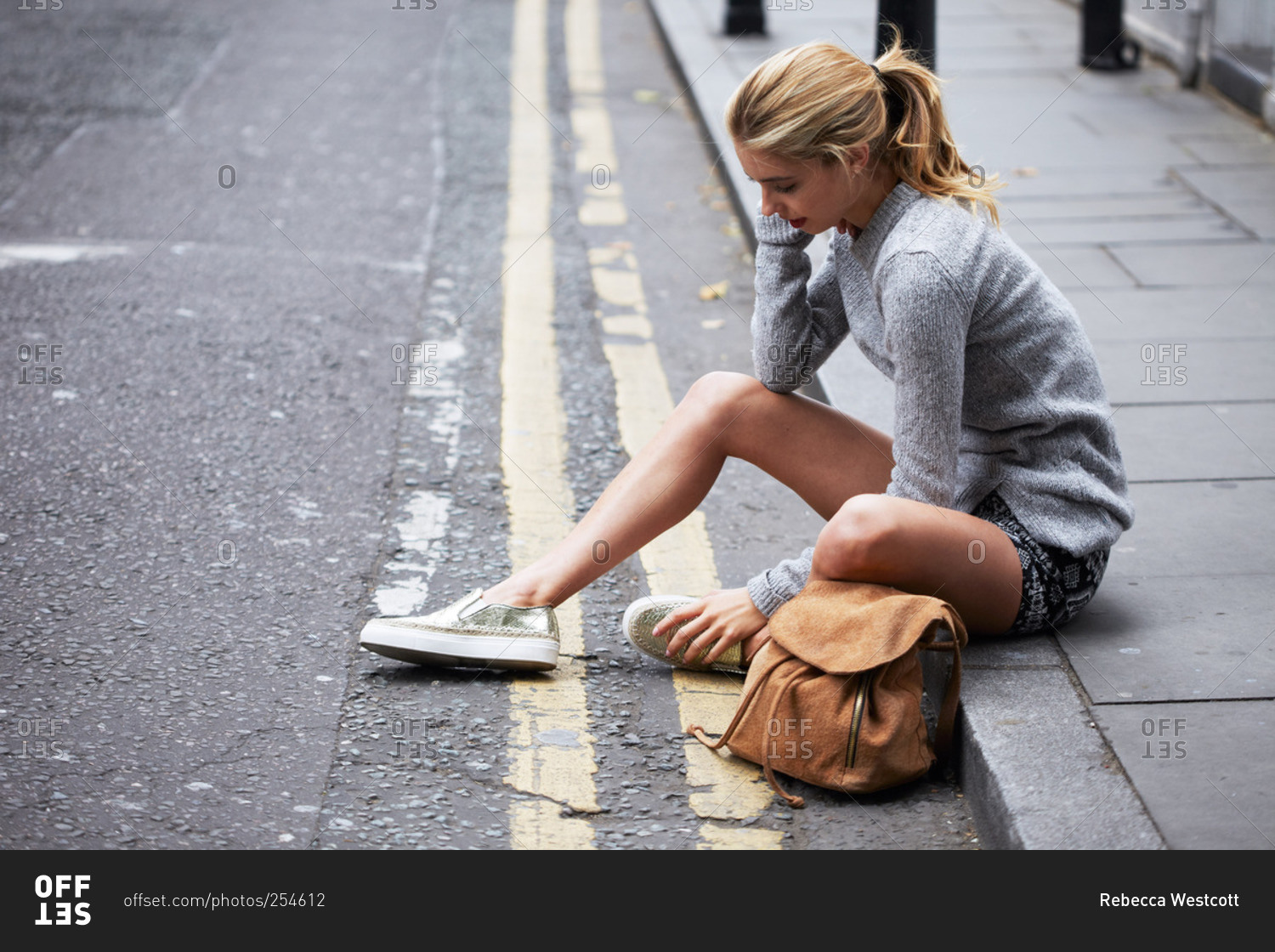 A young woman sits on the sidewalk in a city stock photo OFFSET