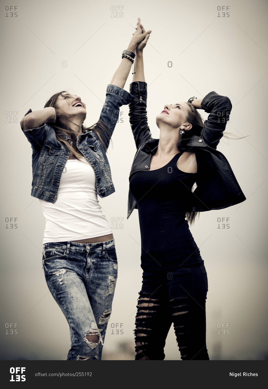 Two young women in ripped jeans hold hands in the air while looking ...