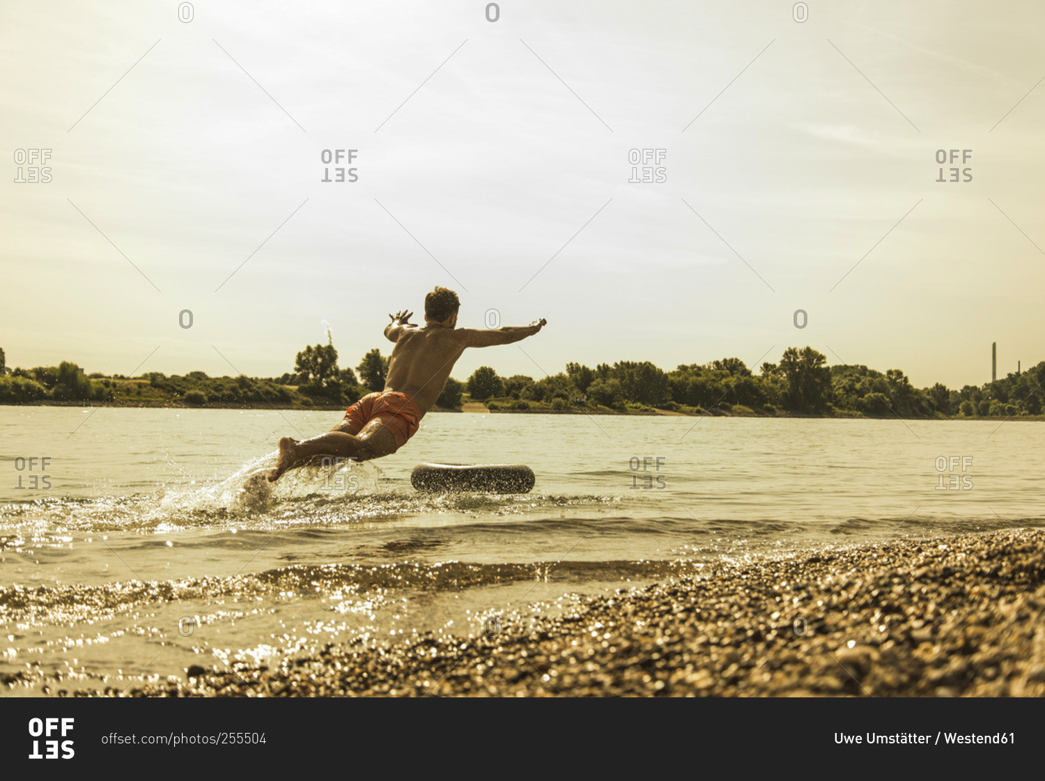 Young man jumping in river with inner tube