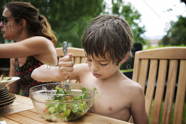 Boy at picnic table poking salad with fork