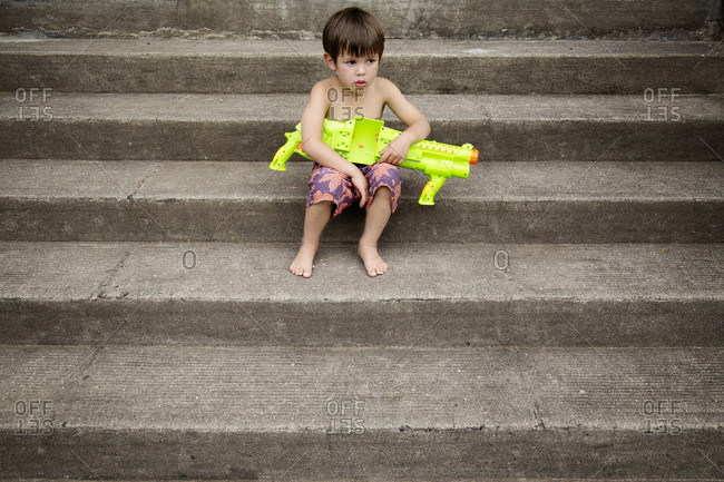 Boy sitting on steps with a water gun