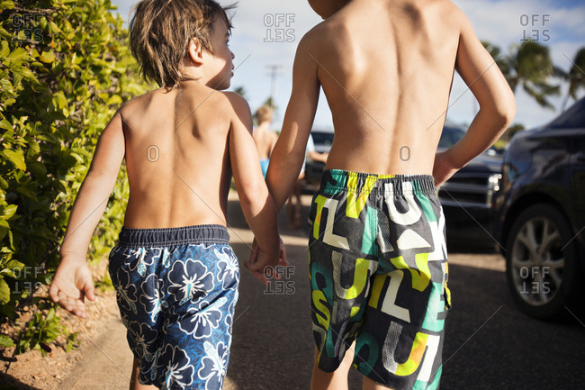 Two boys in swim shorts holding hands walking together