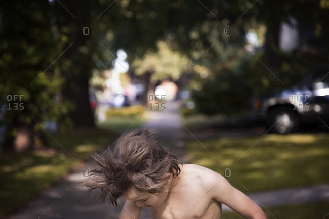 Young boy with messy hair on sidewalk in summer