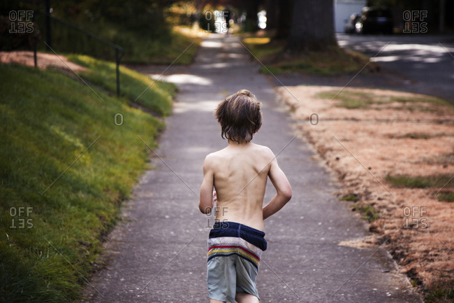 Young boy in swim shorts running down summer sidewalk