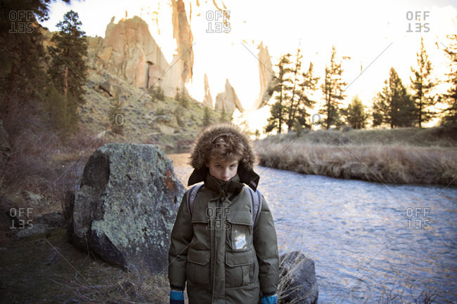 Young boy in parka huddled by river bank