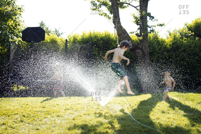 Boy mid air leaping through sprinkler water