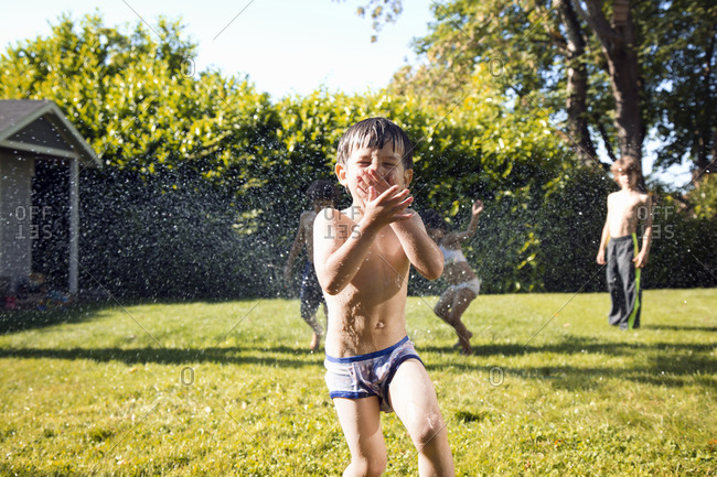 Boy giggling playing in sprinkler
