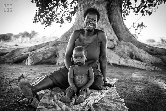 Oroko, Uganda - March 2, 2015: Mother and child sitting on a blanket below a tree